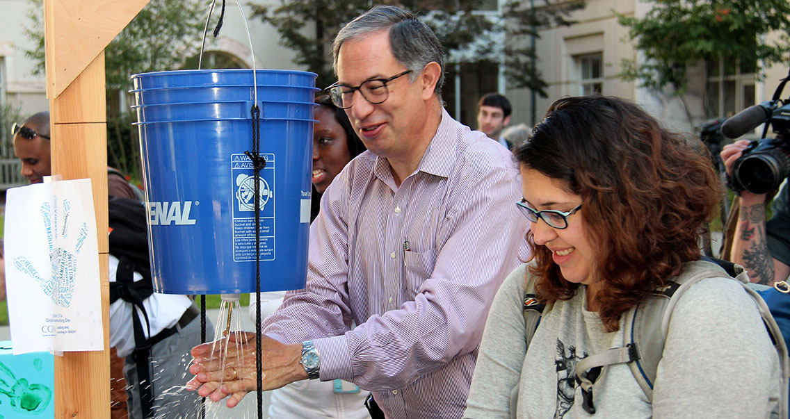 Dr. Carlos Del Rio washes his hands using a jeri-bucket tippy tap during a Global Handwashing Day event